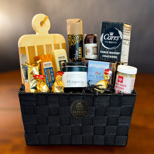 Gift basket with various items including a wooden cutting board, food products, and a bottle of wine on a wooden surface.
