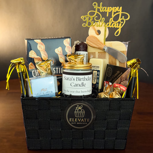 Birthday gift basket with candles, snacks, and a 'Happy Birthday' sign on a wooden surface.